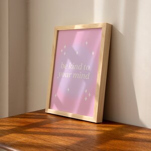 May include: A framed print with a pink and purple gradient background and white diamond shapes. The print says "be kind to your mind".