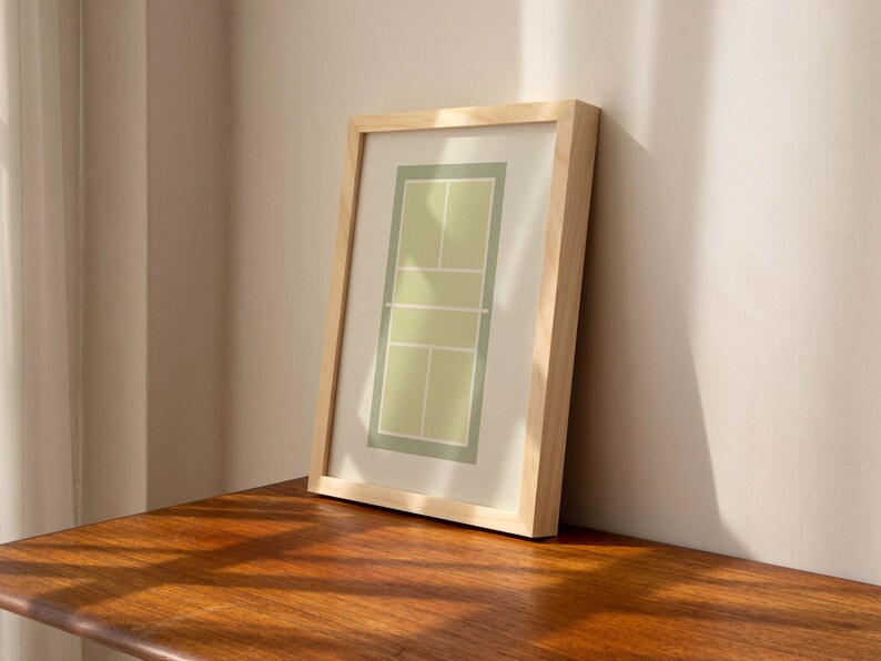 May include: A framed print of a tennis court in green and yellow colors. The frame is made of natural wood.