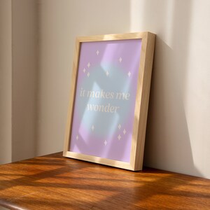 Puede incluir: Una impresi&oacute;n enmarcada con un fondo degradado azul y morado claro y formas de diamantes blancos. El texto "it makes me wonder" est&aacute; impreso en blanco en la impresi&oacute;n.