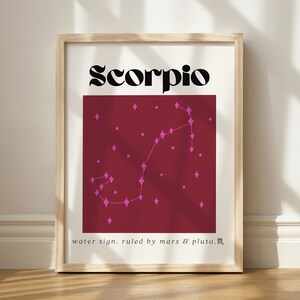 May include: A framed print with a burgundy background and the word "Scorpio" in black text at the top. The constellation Scorpio is depicted in pink with a diamond shape for each star. The text "water sign. ruled by mars & pluto.m" is at the bottom of the print.