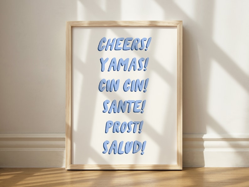 May include: A framed print with the words "Cheers!" "Yamas!" "Cin Cin!" "Sante!" "Prost!" and "Salud!" in blue text on a white background.