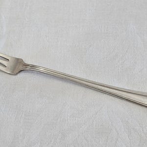 May include: A silver fork with a simple design. The fork has a long, thin handle and a rounded end.
