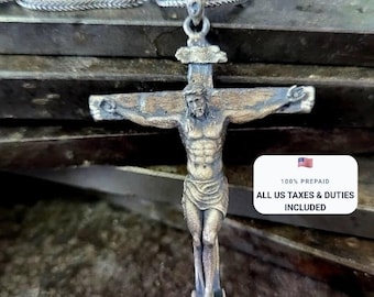 May include: A silver-toned metal crucifix pendant featuring a detailed figure of Jesus on a cross, suspended from a matching silver-toned chain. The pendant has an aged, textured finish with visible dark oxidation in the recessed areas.