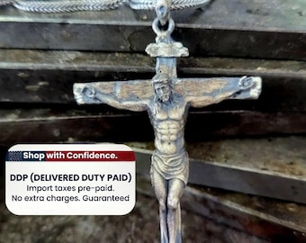 May include: A silver-toned metal crucifix pendant featuring a detailed figure of Jesus on the cross, suspended from a matching silver-toned chain. The pendant has an oxidized finish that highlights the textured details of the figure and cross.