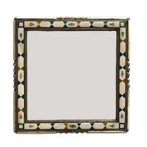 Op de afbeelding: Een vierkante spiegel met een decoratief frame van bot en metaal. Het frame is ingelegd met kleurrijke geometrische patronen in tinten blauw, groen en goud.