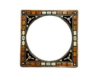 May include: A square, ornate picture frame with a round opening. The frame is made of wood and has a black, white, and brown geometric pattern. The frame is decorated with silver metal accents.