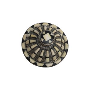 This is a decorative small dish made from a combination of copper and bone. Brass gives it a warm, reflective surface with a hammered texture, while bone inlays add a decorative touch similar to that of ivory, providing a contrast to the metal.