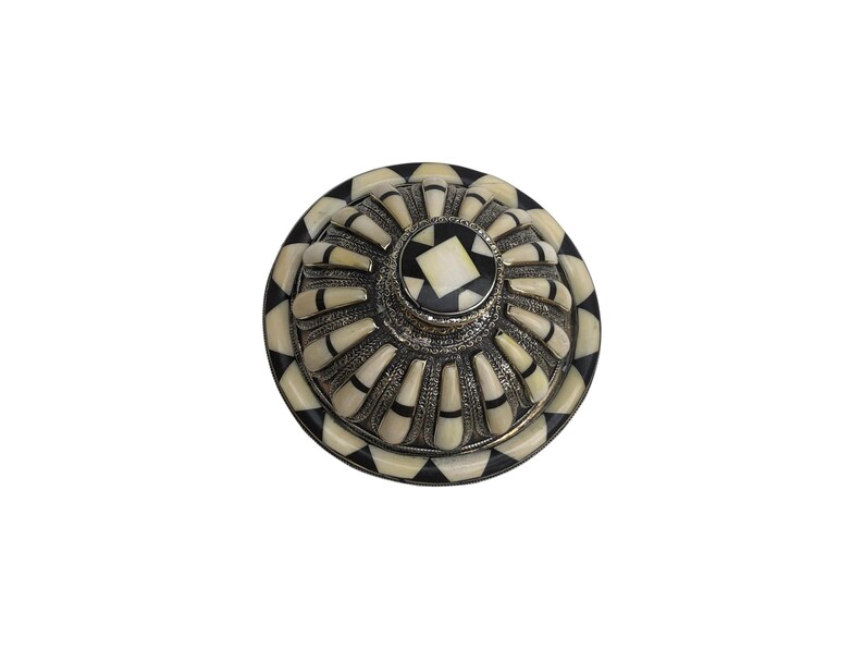 This is a decorative small dish made from a combination of copper and bone. Brass gives it a warm, reflective surface with a hammered texture, while bone inlays add a decorative touch similar to that of ivory, providing a contrast to the metal.
