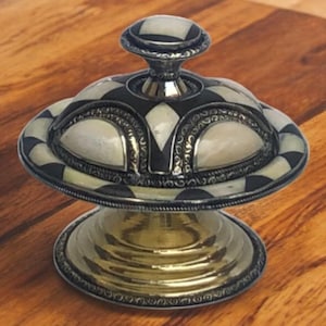 May include: A decorative silver and black lidded box with a geometric pattern and a gold base. The box is made of wood and has a mother of pearl inlay.