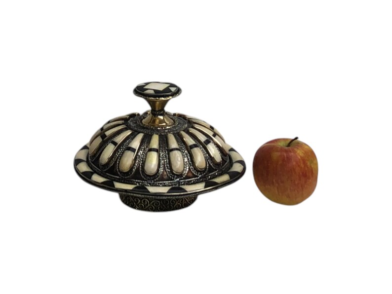This is a decorative small dish made from a combination of copper and bone. Brass gives it a warm, reflective surface with a hammered texture, while bone inlays add a decorative touch similar to that of ivory, providing a contrast to the metal.