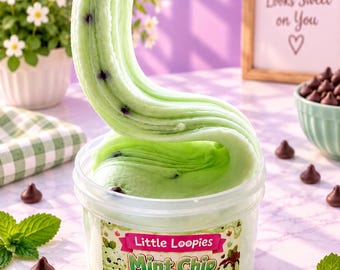 Puede incluir: Un recipiente de plástico transparente lleno de slime de color verde claro con chispas de chocolate, con una parte del slime estirada hacia arriba. La etiqueta del recipiente muestra el texto Little Loopies Mint Chip Ice Cream con dibujos.
