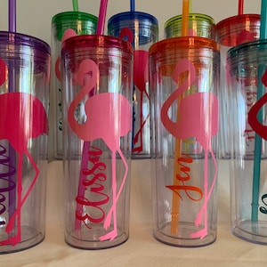 May include: Set of six clear plastic tumblers with colorful lids and straws. Each tumbler features a pink flamingo silhouette and a personalized name: Kellie, Elissa, Jen, Jamie, and two others.