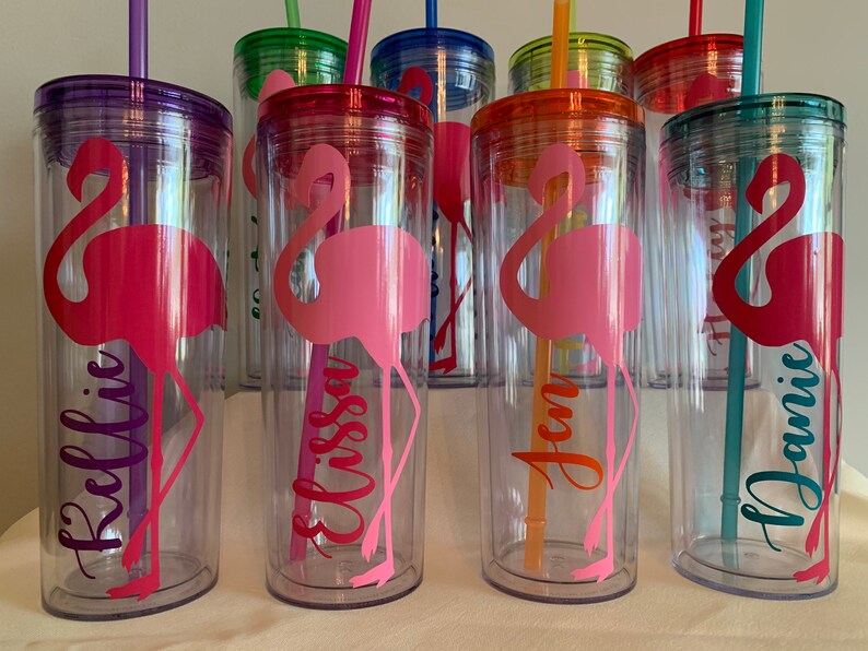 May include: Set of six clear plastic tumblers with colorful lids and straws. Each tumbler features a pink flamingo silhouette and a personalized name: Kellie, Elissa, Jen, Jamie, and two others.