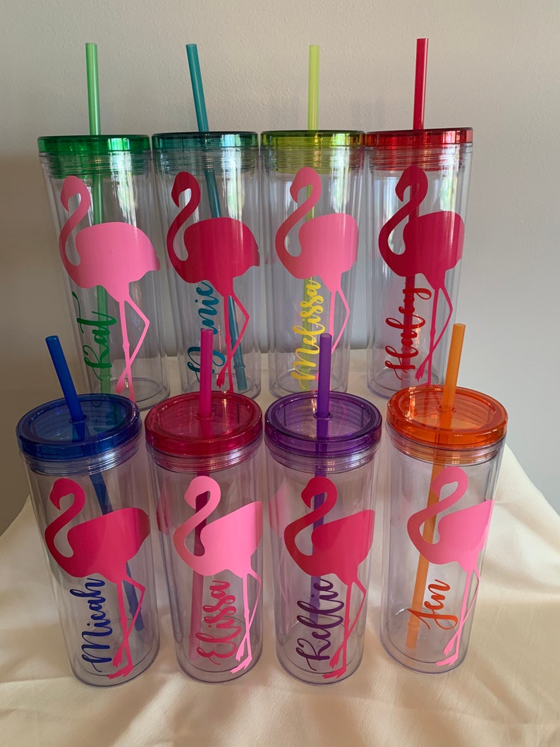 May include: Set of eight clear plastic tumblers with colorful lids and straws. Each tumbler features a pink flamingo silhouette and a personalized name, including:  'Kai', 'Monica', 'Melissa', 'Holly', 'Michaela', 'Elissa', 'Kellie', and 'Jen'.