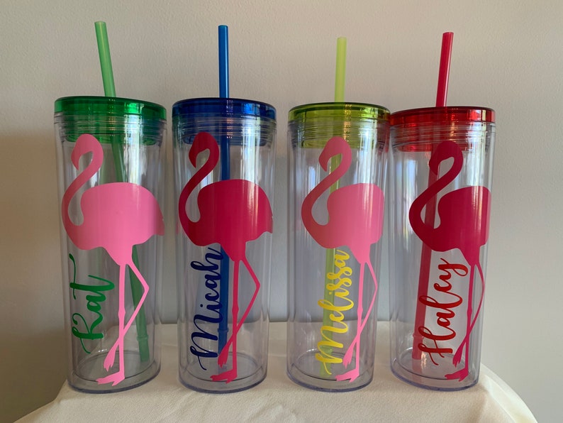 May include: Four clear plastic tumblers with pink flamingo designs and personalized names:  Kat, Micah, Melissa, and Haley. Each tumbler has a matching colored lid and straw.