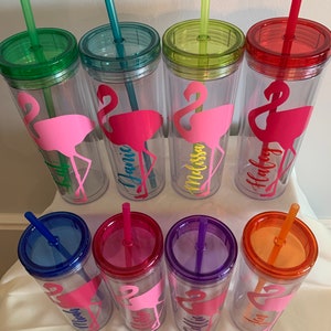 May include: Set of ten clear plastic tumblers with colorful lids and straws. Each tumbler features a pink flamingo silhouette and a personalized name, including "Jamie", "Melissa", "Holly", "Mia", "Ellie", "Kallie", and "Ann".