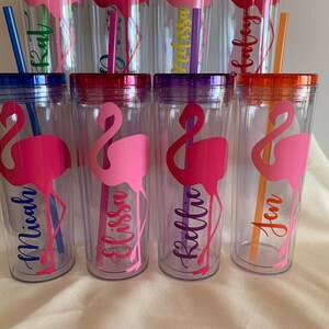 May include: Six clear plastic tumblers with colorful lids and straws. Each tumbler features a pink flamingo silhouette and a personalized name: Micah, Elissa, Kelli, Jen, Kat, and Alyssa.