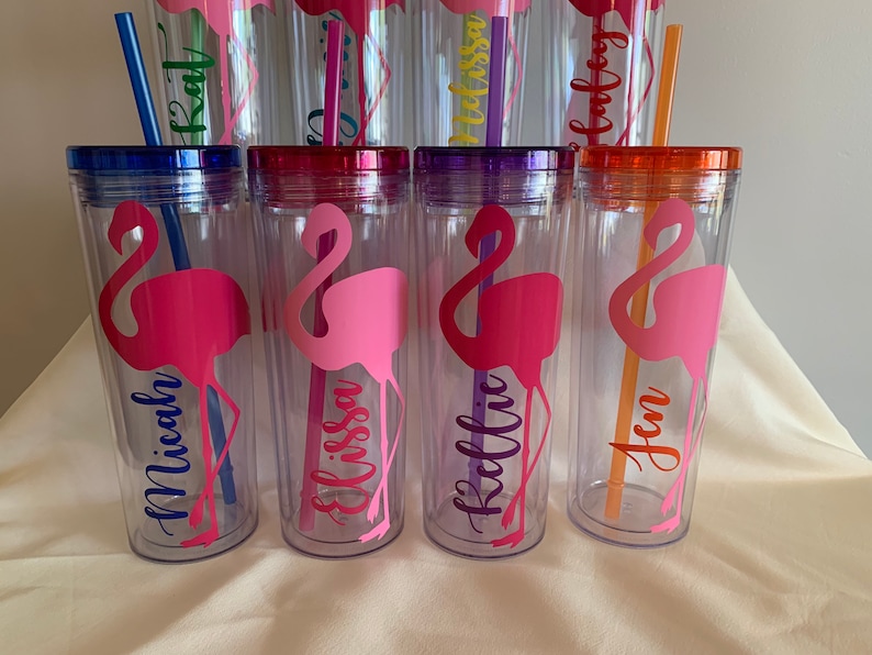 May include: Six clear plastic tumblers with colorful lids and straws. Each tumbler features a pink flamingo silhouette and a personalized name: Micah, Elissa, Kelli, Jen, Kat, and Alyssa.