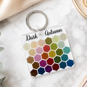 May include: A square acrylic keychain featuring a grid of colorful hexagons in various shades of green, blue, red, yellow, and purple. The text Dark Autumn is printed in black script at the top, and a silver metal split ring is attached to the top.