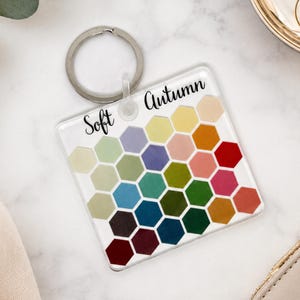 May include: A square acrylic keychain featuring a grid of colorful hexagons in various shades of green, blue, red, and yellow. The text Soft Autumn is printed in black script at the top. The keychain includes a silver metal split ring for attachment.