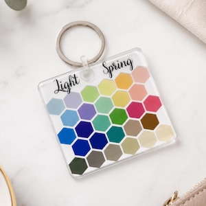 May include: A square clear acrylic keyring featuring a grid of multicoloured hexagons in various shades. The text Light Spring is printed in black script at the top. The keyring includes a silver metal split ring attached to the top centre.
