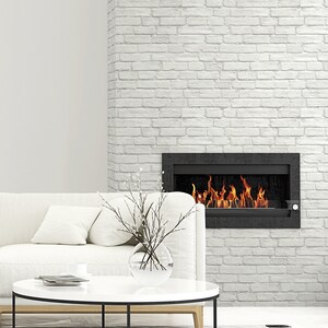 May include: A rectangular black fireplace insert with visible orange and yellow flames is mounted on a white brick wall. A white sofa with cushions sits in front of the fireplace, accompanied by a round white coffee table with a glass vase.