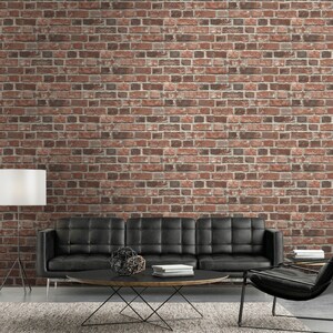 May include: A black tufted sofa sits in front of a red brick wall. A round black coffee table with a metal base holds a geometric sculpture and a stack of books. A floor lamp with a white shade stands to the left, and a black chair is on the right.