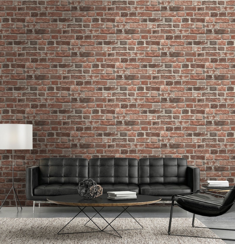 May include: A black tufted sofa sits in front of a red brick wall. A round black coffee table with a metal base holds a geometric sculpture and a stack of books. A floor lamp with a white shade stands to the left, and a black chair is on the right.