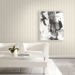 K&ouml;nnte beinhalten: Ein quadratisches gerahmtes Wandbild mit einer abstrakten Schwarz-Wei&szlig;-Tuschmalerei mit kr&auml;ftigen, ausdrucksstarken Pinselstrichen. Das Kunstwerk befindet sich in einem d&uuml;nnen wei&szlig;en Rahmen und h&auml;ngt an einer Wand mit beigefarbener Streifentapete.
