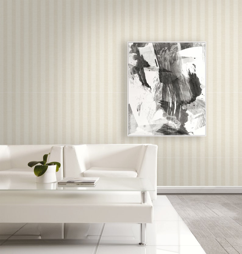 K&ouml;nnte beinhalten: Ein quadratisches gerahmtes Wandbild mit einer abstrakten Schwarz-Wei&szlig;-Tuschmalerei mit kr&auml;ftigen, ausdrucksstarken Pinselstrichen. Das Kunstwerk befindet sich in einem d&uuml;nnen wei&szlig;en Rahmen und h&auml;ngt an einer Wand mit beigefarbener Streifentapete.