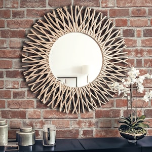 May include: A round wall mirror featuring a decorative frame composed of numerous thin, curved metallic rods arranged in a sunburst pattern. The mirror has a reflective glass centre and is mounted on a wall with a textured red brick surface.