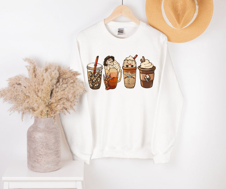 May include: White sweatshirt with a graphic of four different coffee drinks. The drinks include a pumpkin spice latte, a caramel macchiato, a peppermint mocha, and a regular coffee.