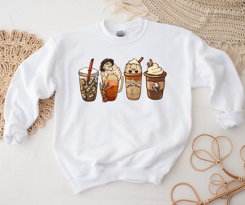 May include: White sweatshirt with a graphic of four different coffee drinks. The drinks are a pumpkin spice latte, a caramel macchiato, a mocha, and a regular coffee. Each drink has a spooky Halloween character on it.