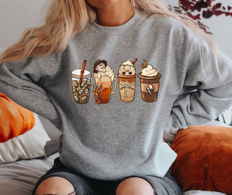 May include: A gray sweatshirt with a graphic of four different coffee drinks. The drinks are decorated with Halloween-themed characters, including a ghost, a pumpkin, and a vampire.