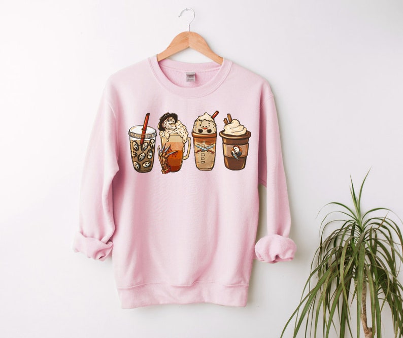 May include: Pink sweatshirt with a graphic of four different coffee drinks with whipped cream and toppings. The drinks are in a row from left to right.