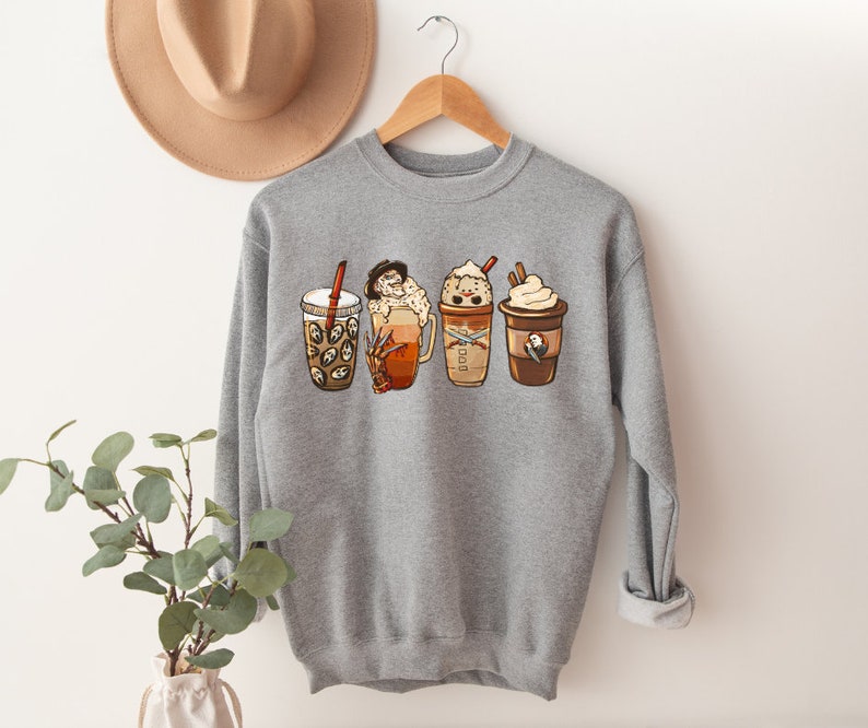 May include: Gray sweatshirt with a graphic of four different coffee drinks with whipped cream and toppings. The drinks are arranged in a row from left to right.