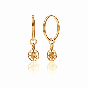 May include: Gold hoop earrings with a small compass charm hanging from each hoop.