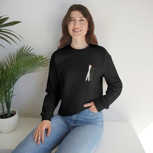 Könnte beinhalten: Ein schwarzes Sweatshirt mit einer kleinen Grafik von zwei weißen Skistöcken mit orangenen Spitzen auf der linken Brust.