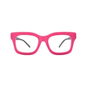 May include: Bright pink eyeglasses featuring a thick, bold frame with a matte, textured finish. The glasses have clear lenses and dark, slender temples that extend from the sides of the frame, providing a distinct contrast to the vibrant pink front.