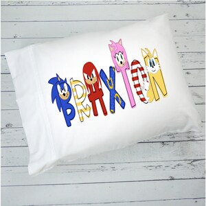 May include: White pillowcase with the name "Brayton" spelled out in colorful letters. Each letter features a different character from the Sonic the Hedgehog video game series.