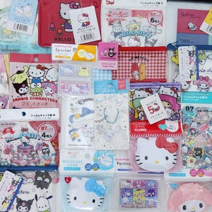 Peut inclure: Une collection de produits dérivés Hello Kitty et Sanrio, comprenant des pochettes, des étuis et des autocollants. Les articles présentent divers motifs avec les personnages emblématiques aux couleurs vives. Certains articles ont du texte et des étiquettes en japonais.