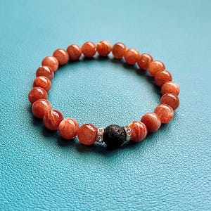 May include: A bracelet made of orange sunstone beads with a black lava rock bead and silver accents.
