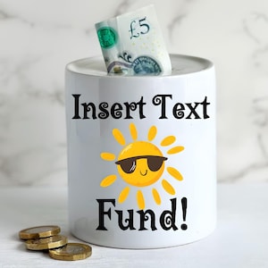 May include: White ceramic money box with a smiling sun wearing sunglasses. The text "Insert Text Fund!" is printed on the front of the money box.