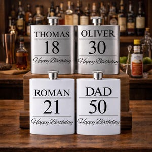 May include: Four hip flasks, two silver and two white, with black text. The flasks are inscribed with names, ages, and "Happy Birthday". Measurements are not applicable.