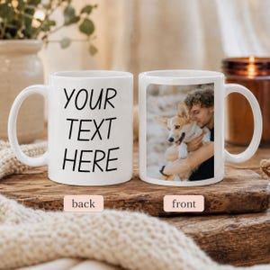 May include: Two white ceramic mugs with handles. The left mug features the black text YOUR TEXT HERE. The right mug displays a photographic print of a person holding a light brown and white Corgi dog. The mugs are positioned side by side.