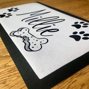 May include: White doormat with black border and black paw prints and bone design. The name "Millie" is written in black cursive.