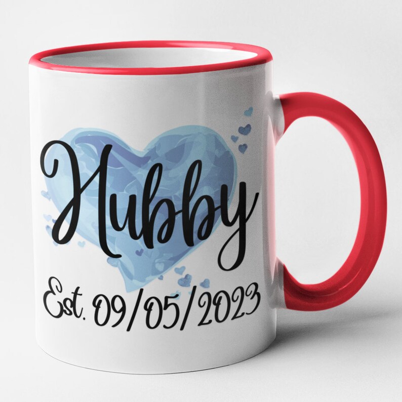 May include: White ceramic mug with a red rim and handle. The mug features a blue watercolor heart with the word "Hubby" in black script. Below the heart is the text "Est. 09/05/2023".