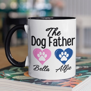 May include: White ceramic mug with a black rim and handle. The mug has the text "The Dog Father" with two paw print hearts, one pink and one blue, and the names "Bella" and "Alfie" underneath.