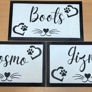 May include: Three black framed white mats with black paw print hearts and a cat face design. The mats have the names "Boots", "Cosmo", and "Gizmo" written in black cursive.