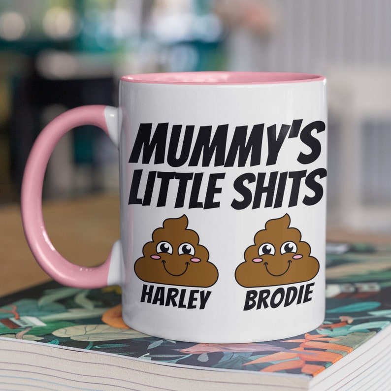 May include: White ceramic mug with a pink rim and handle. The mug has a black graphic that says "Mummy's Little Shits" with two cartoon poop emojis with faces. The poop emojis are labeled "Harley" and "Brodie".